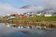 Picturesque Qeqertarsuaq village reflecting on a tranquil lake in Greenland under a cloudy sky.