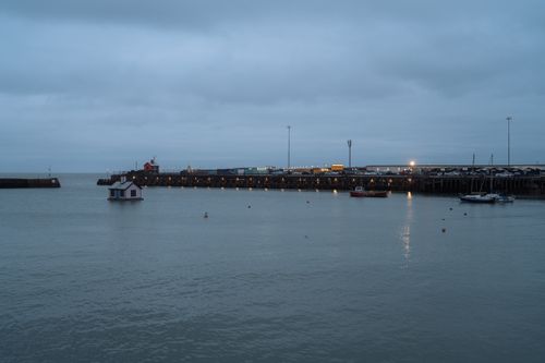 Free A peaceful coastal harbor scene at twilight with boats and lights reflecting on calm waters. Stock Photo