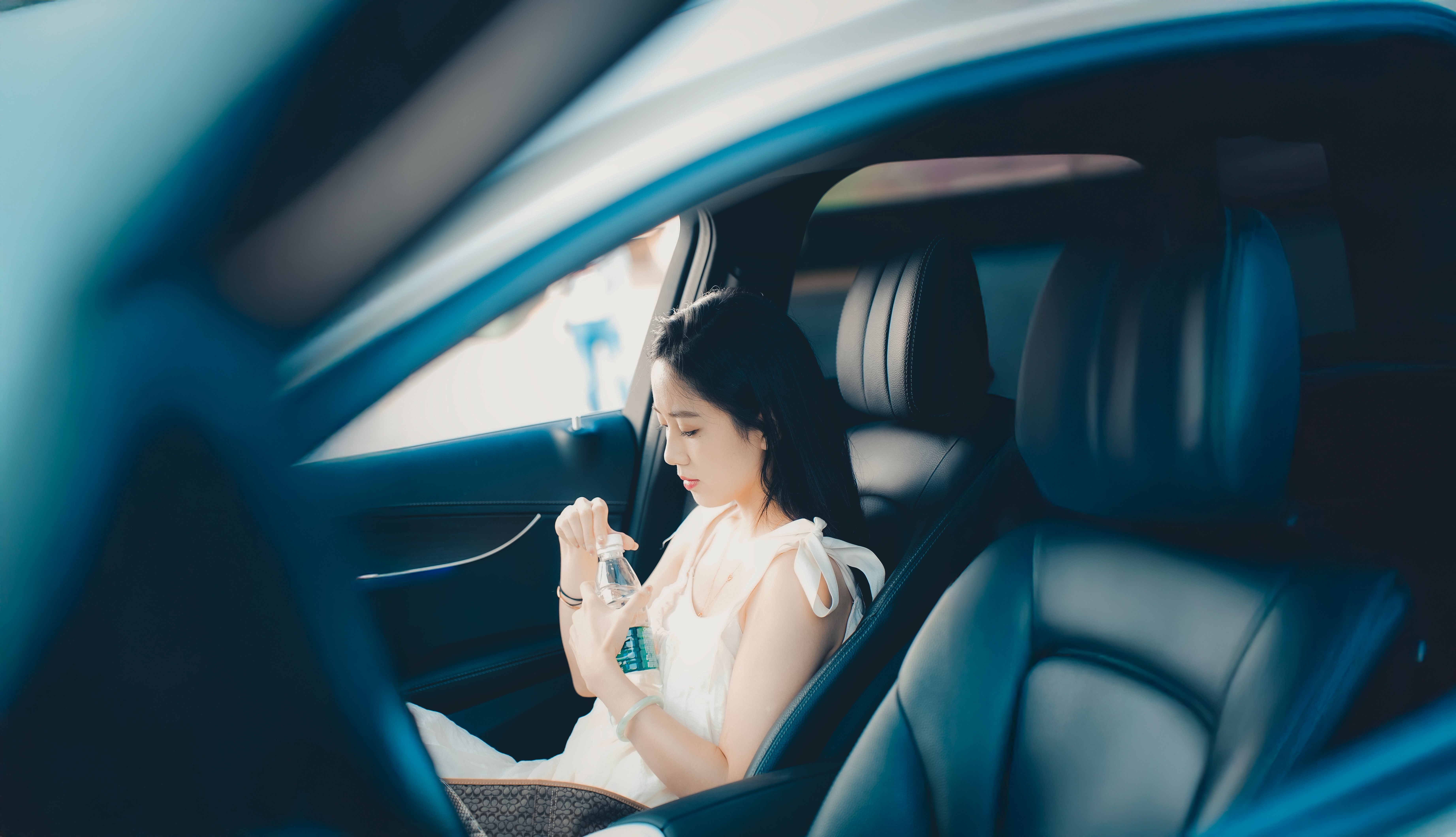 Woman in a white dress sipping a refreshing drink while seated inside a car in daylight.