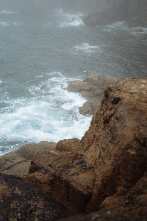 Free Captured coastal scenery with rugged rocks, ocean waves, and fog creating a moody and serene atmosphere. Stock Photo