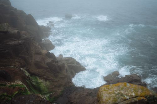 Free Fog envelops a dramatic rocky coastline in England, showcasing nature's untamed beauty. Stock Photo
