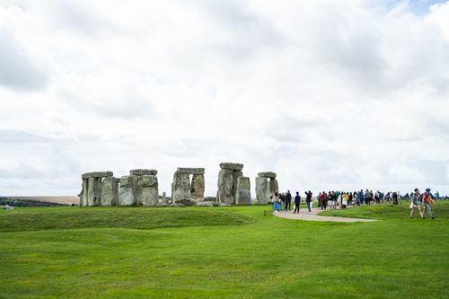 Free Tourists visit Stonehenge, under a cloudy sky, in England's green landscape. Stock Photo