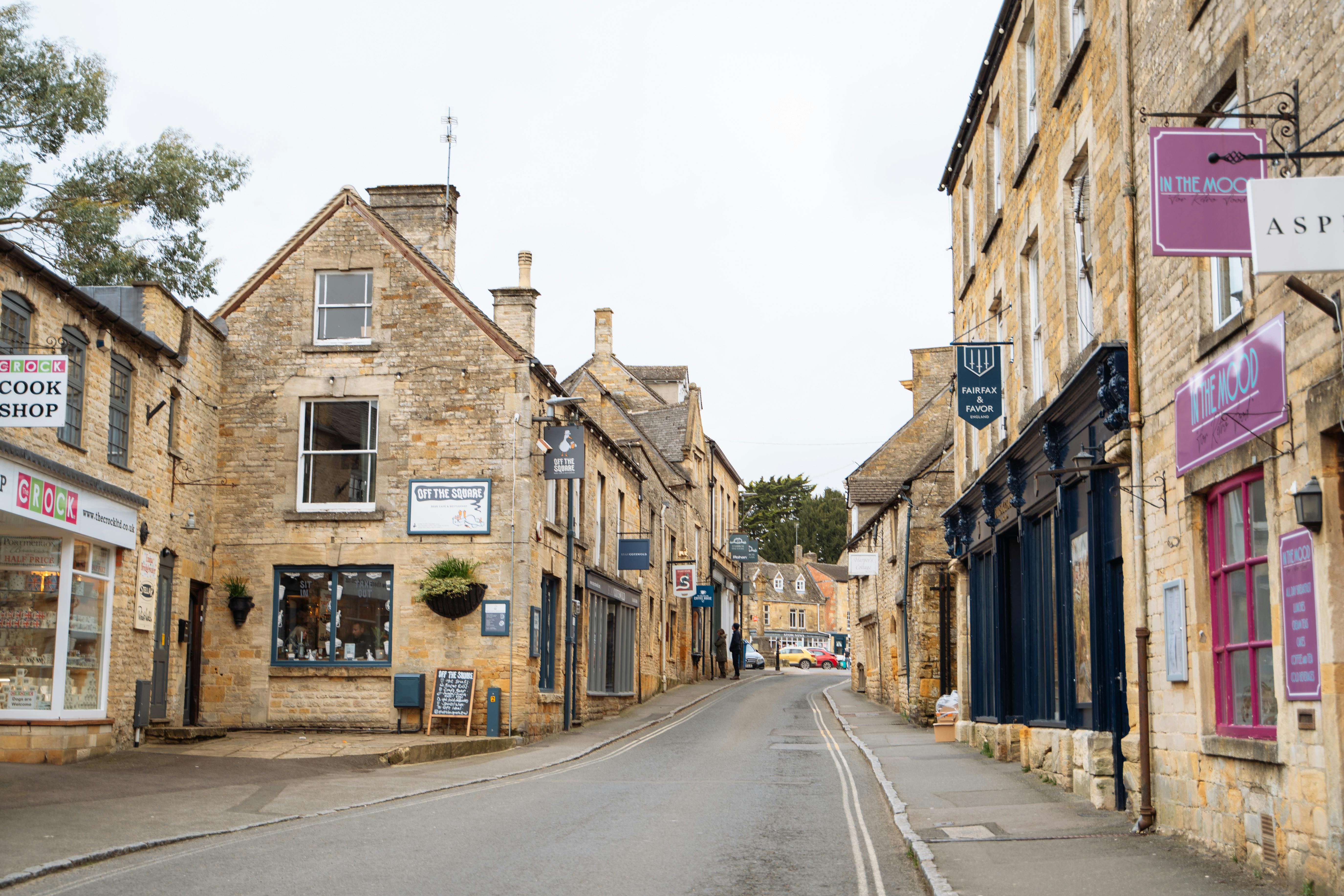 Picturesque village street in the Cotswolds, England featuring historic stone buildings and quaint shops.