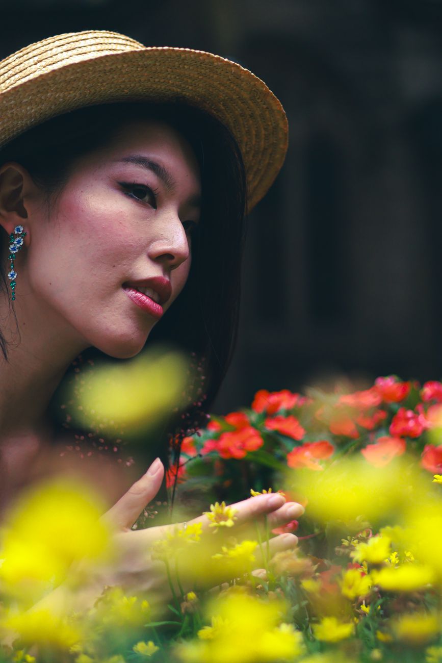 A stylish woman in a straw hat poses among colorful flowers in an outdoor setting. Captured in Sydney.