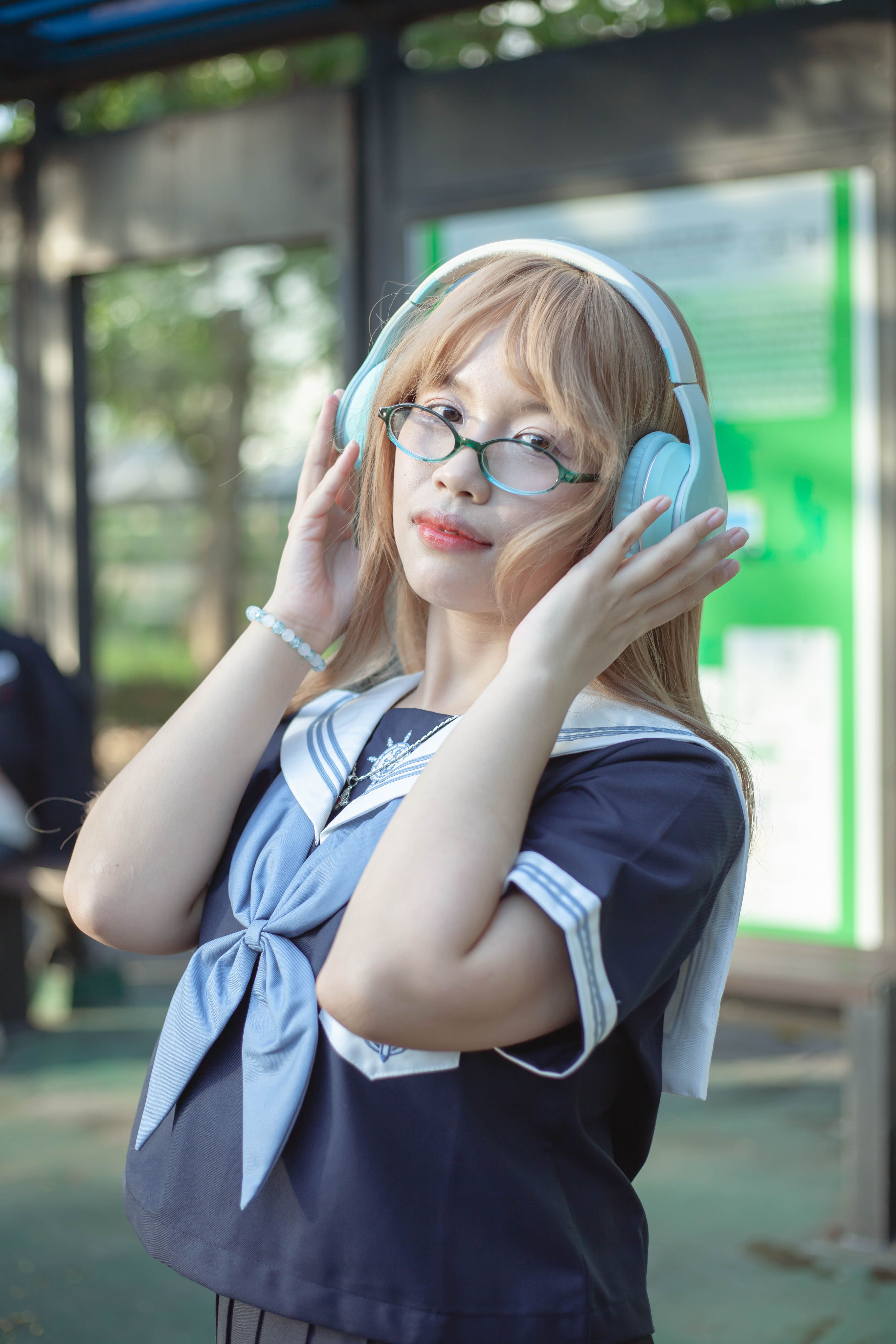 Young woman in a sailor-style school uniform listening to music with headphones outdoors.