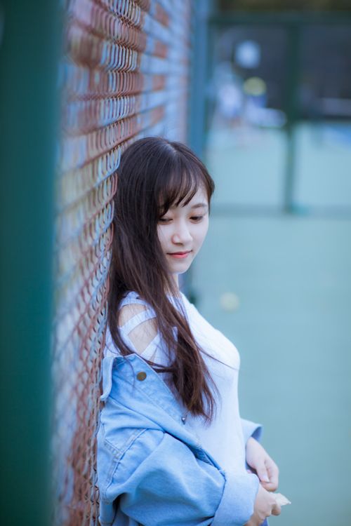 Free A young woman in casual clothing leans on a chain-link fence, looking serene. Stock Photo