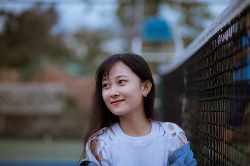 Free Young woman standing by tennis court net looking cheerful outdoors. Stock Photo