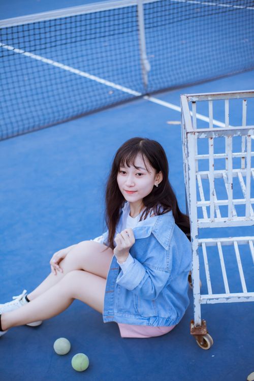 Free A young woman in casual attire sits on a tennis court next to a ball cart. Stock Photo