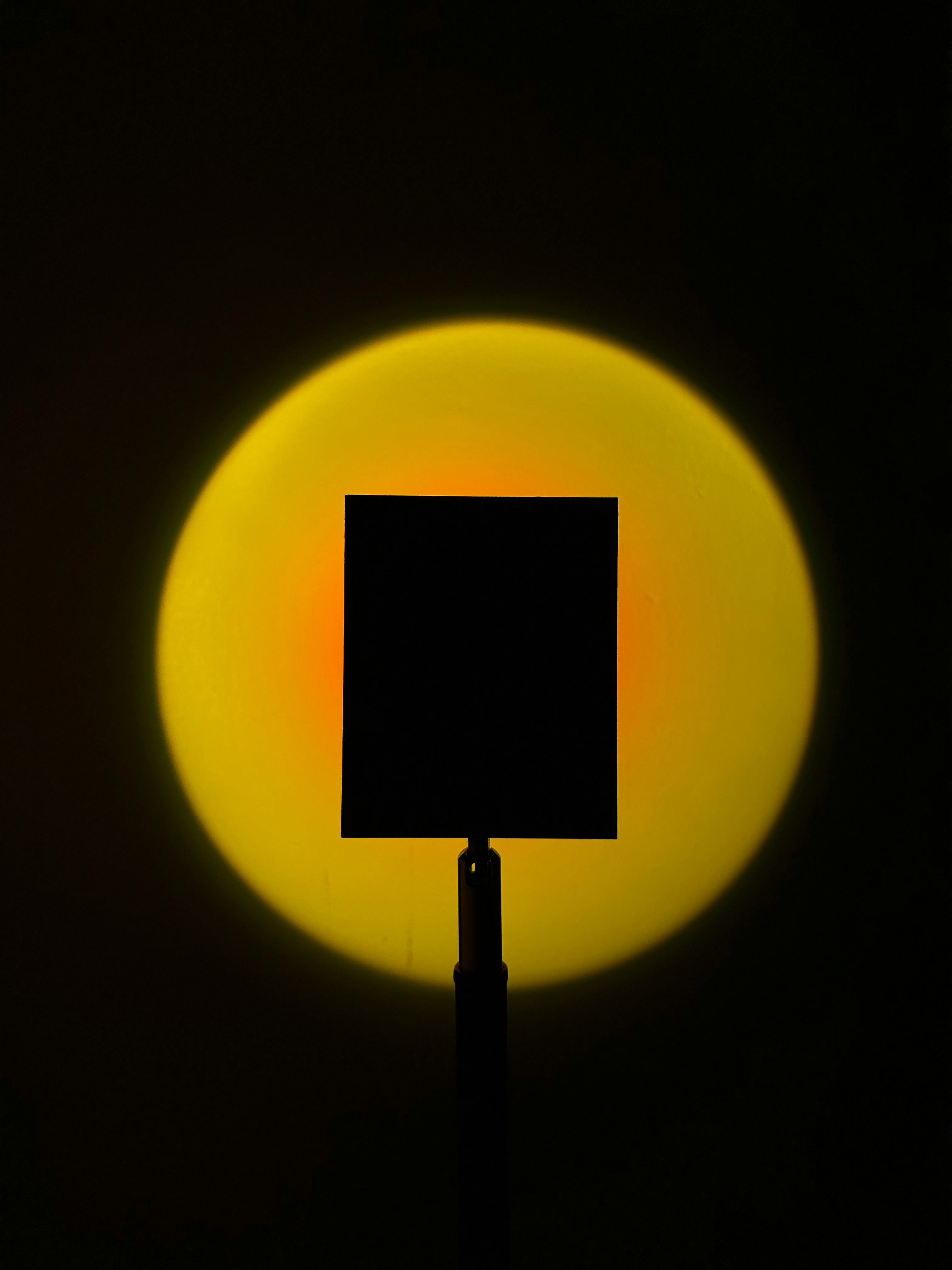 gratis Silhouet van een vierkante vorm tegen een gloeiende gele cirkel op een donkere achtergrond. Stockfoto