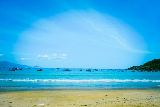 A serene beach with calm waters and boats under a clear blue sky, ideal for relaxation.