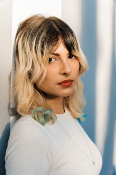 Contemporary portrait of a young adult with blonde hair and septum piercing, wearing a white top.
