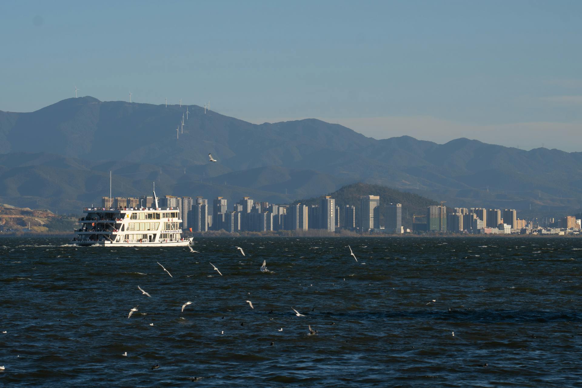 A picturesque view of a ferry on Dali Lake with mountains and a city skyline in the background.