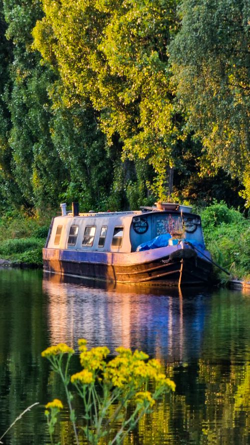 Free Peaceful canal boat reflecting in water surrounded by autumn foliage. Stock Photo