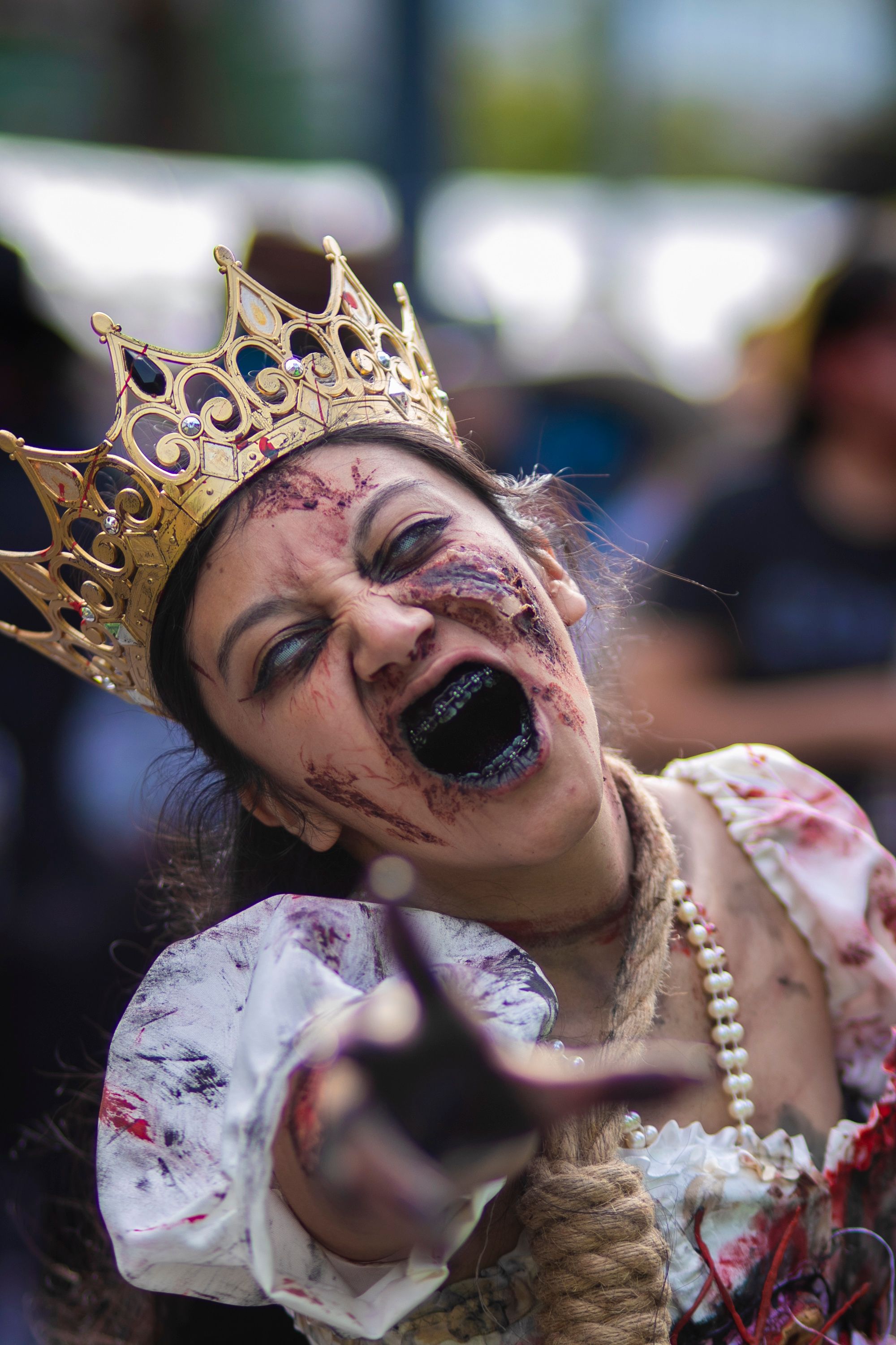 A zombie queen in costume with a crown at an outdoor cosplay event, reaching out dramatically.