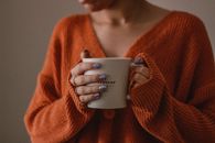 Woman in orange sweater holding a warm coffee cup indoors on a cozy fall morning.