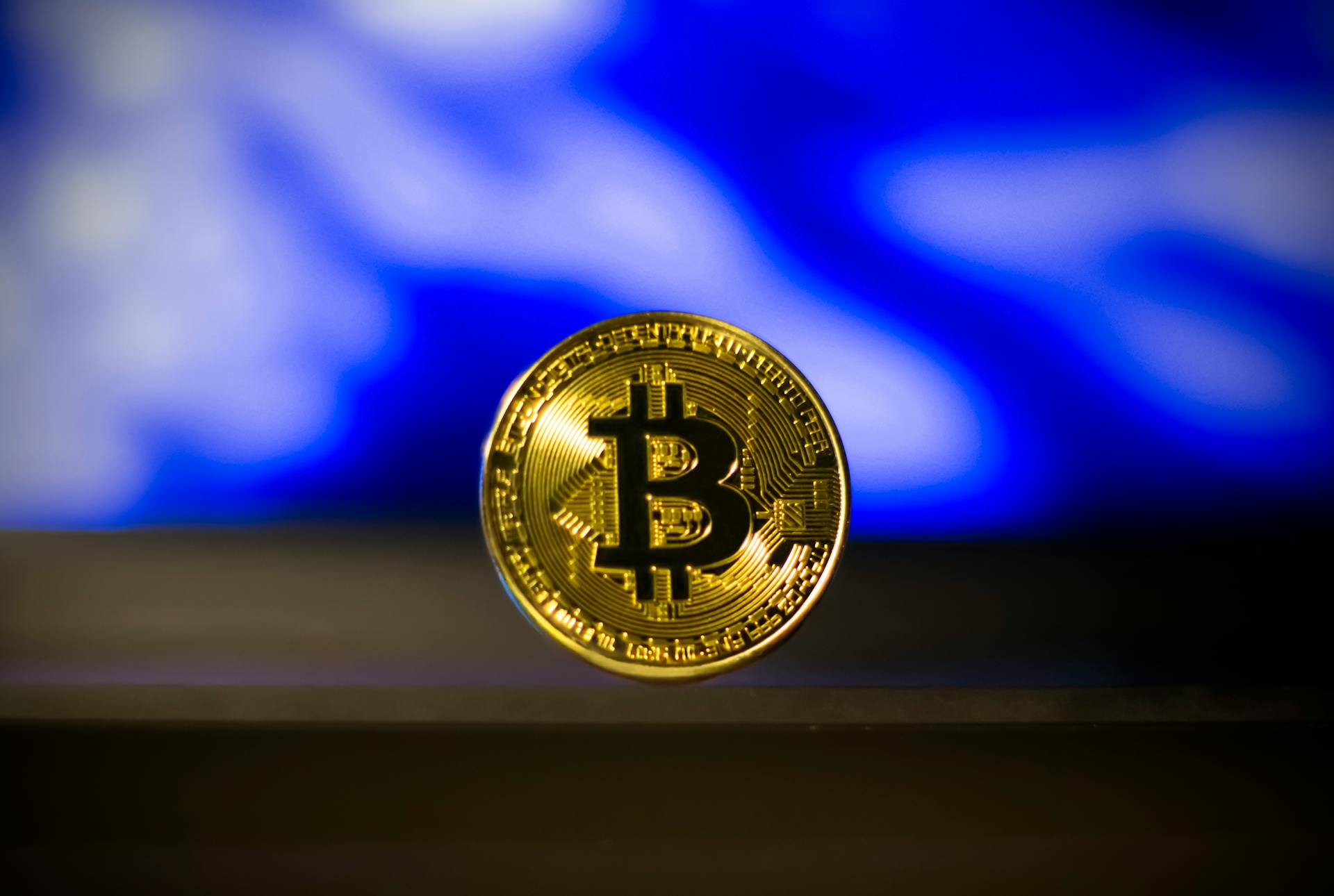 Close-up of a golden Bitcoin coin with a blurred blue abstract background, symbolizes digital currency.