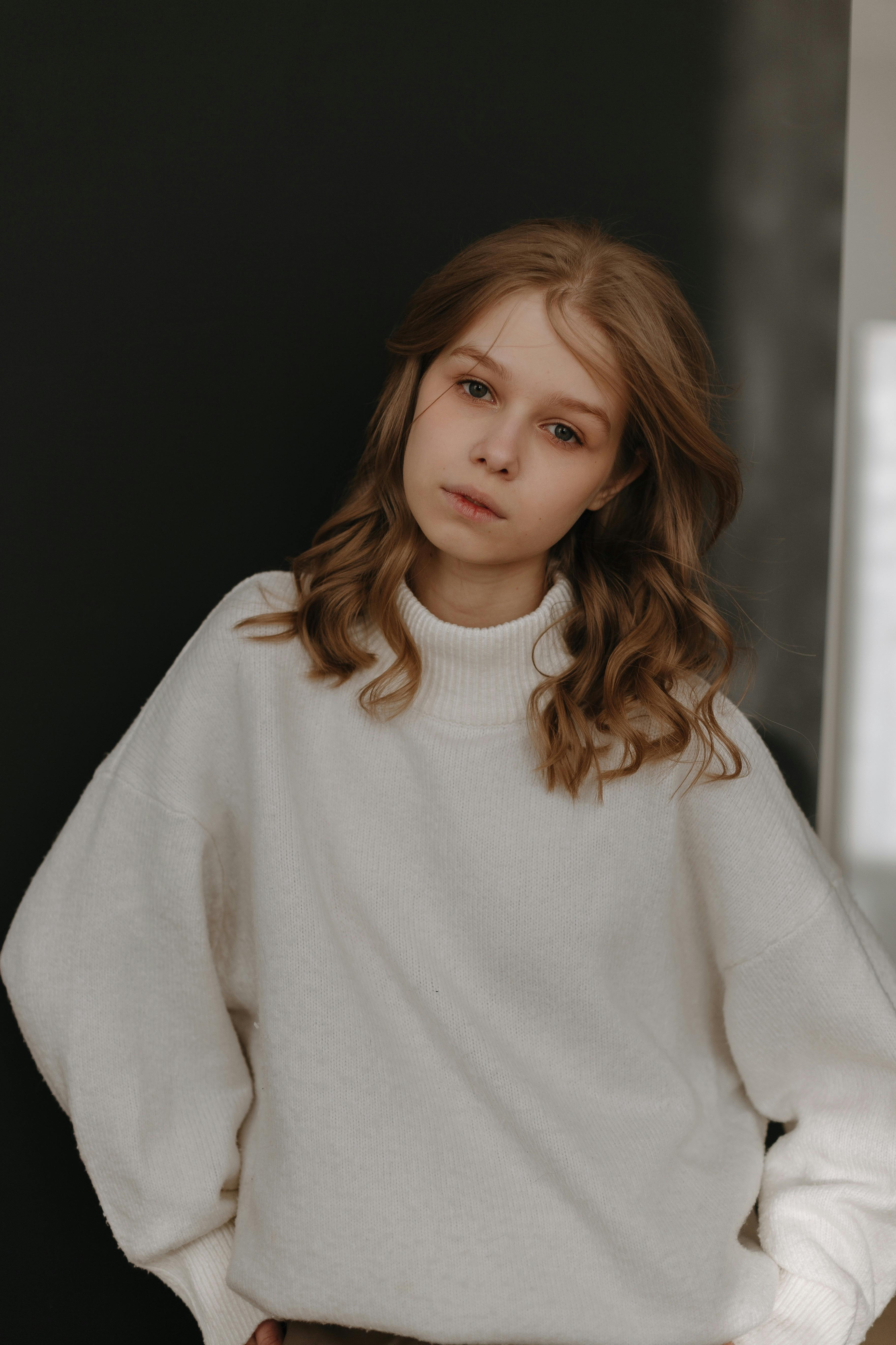 Serene portrait of a young woman in a warm white sweater against a dark background.