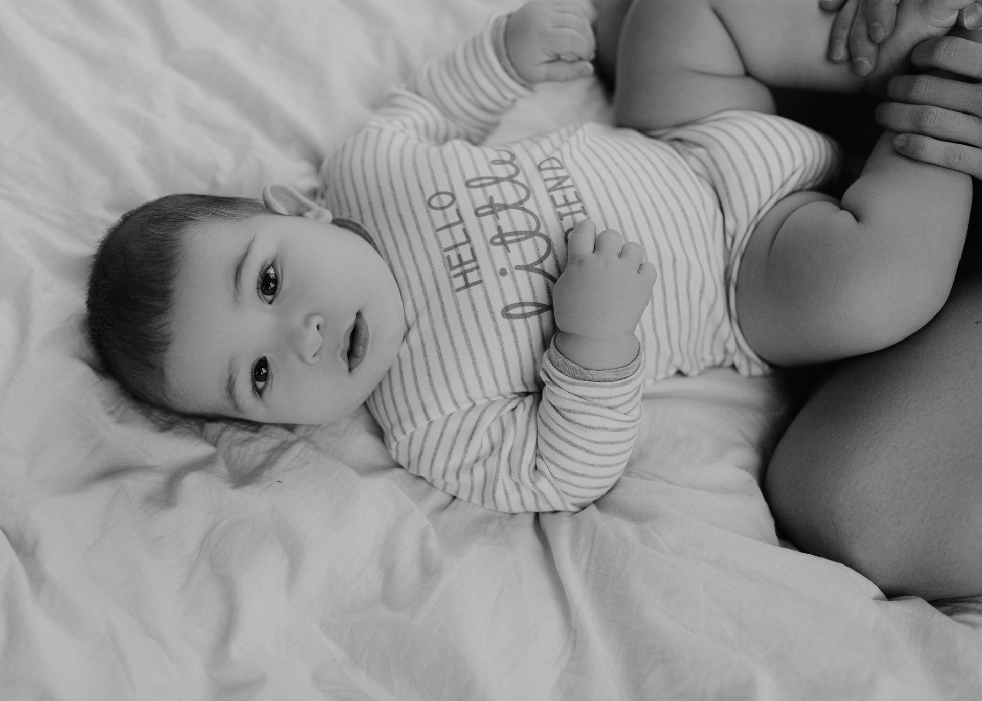 Black and white photo of a cute baby lying on a bed, with a cozy atmosphere.