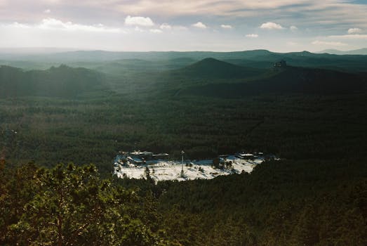 A breathtaking aerial shot of Kazakhstan's forested mountains with a distant building.