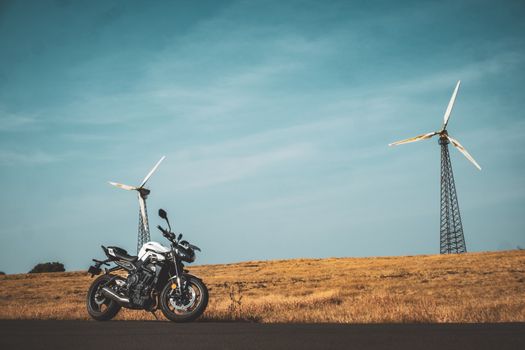 A motorcycle parked in an open field with wind turbines under a clear blue sky in India, showcasing adventure and renewable energy.