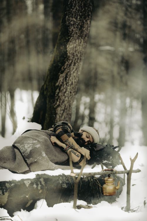 Camper resting under a thick insulating blanket beside a sleeping bag and pack in a snow-covered winter forest, illustrating how sleeping bag temperature ratings relate to overnight warmth in cold conditions