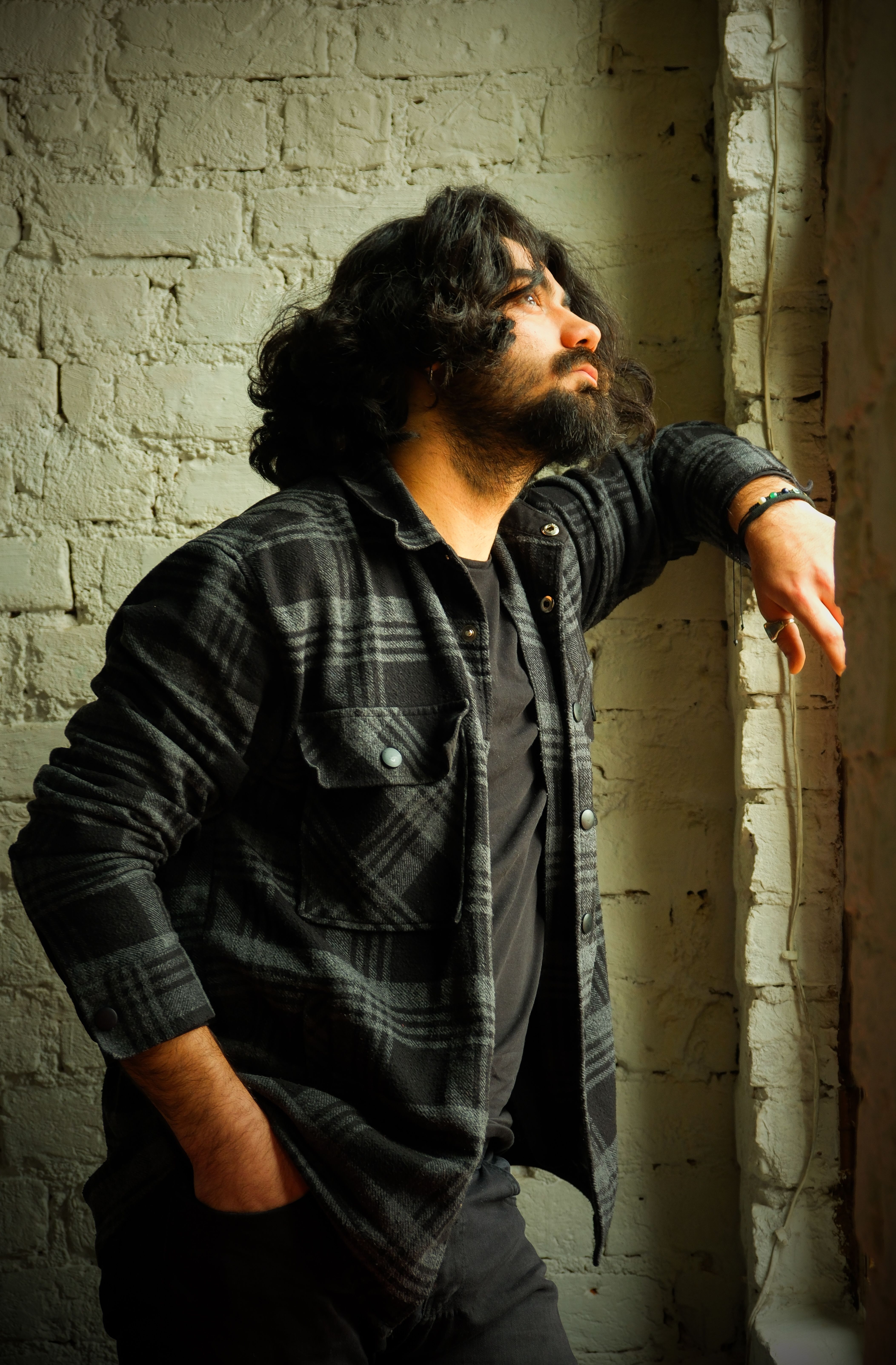 Reflective bearded man in plaid shirt gazing out window in a rustic setting.