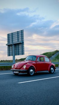 A classic red car cruises on a highway at dusk, capturing a nostalgic road trip moment.