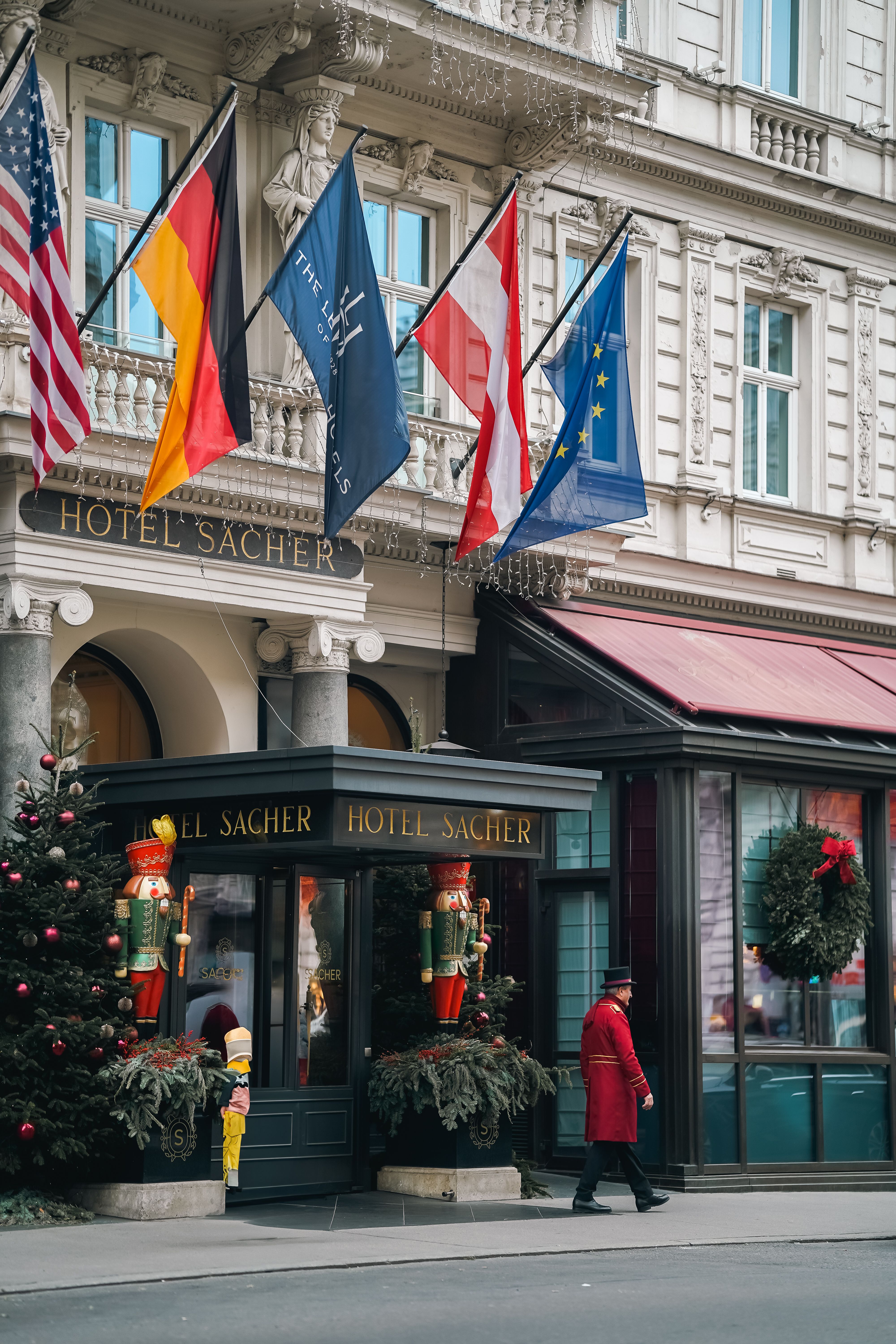 Elegant winter exterior of Hotel Sacher in Vienna, adorned with festive decorations and national flags.