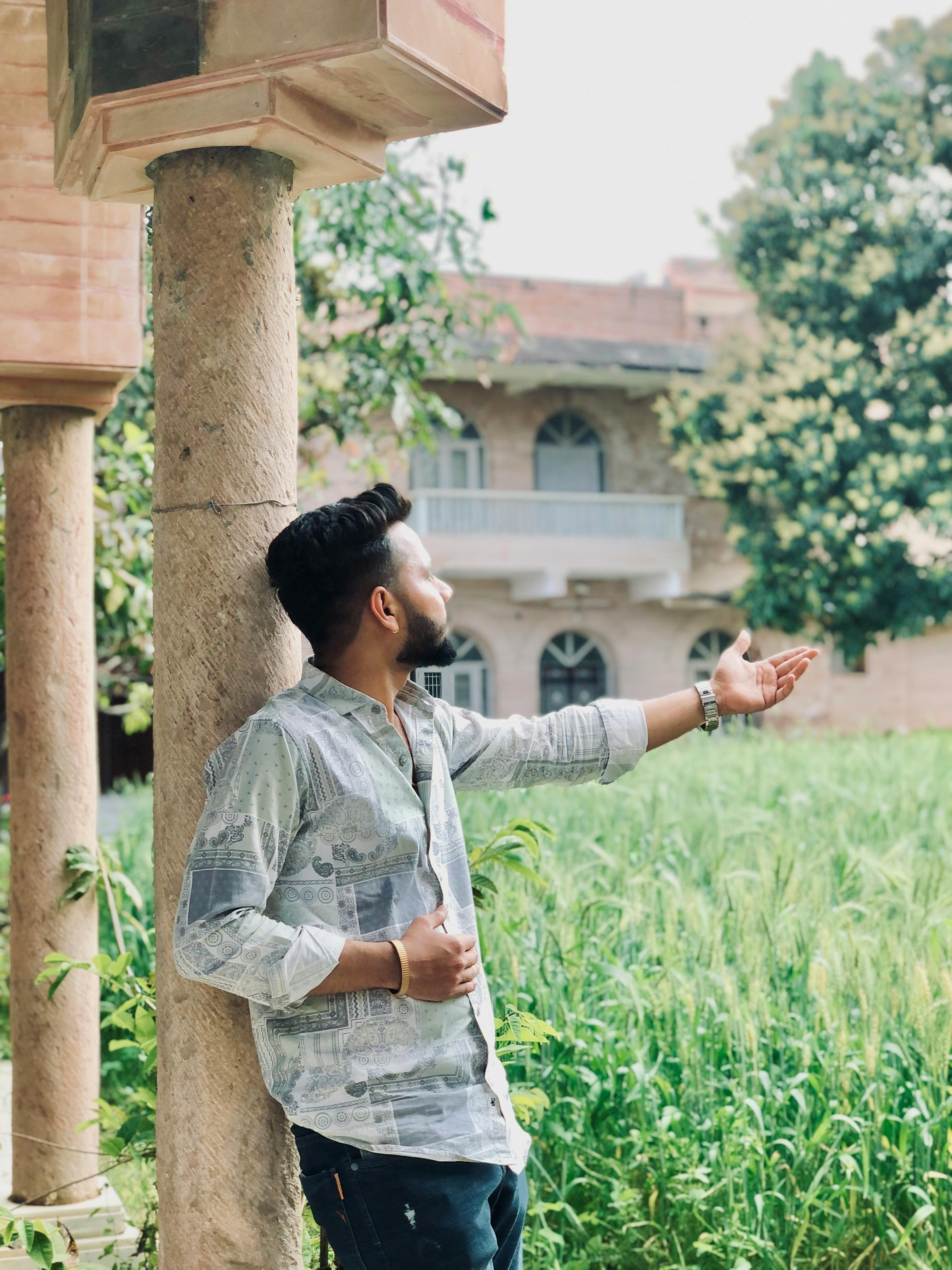 Young man posing outdoors near historic architecture with lush greenery.