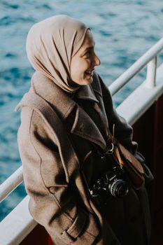 A woman wearing a hijab and a coat enjoying a boat ride in Istanbul, Türkiye.