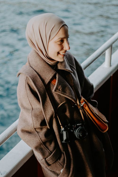 Free A woman in a hijab enjoys the view on a boat, with the sea in the background. Stock Photo