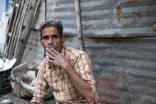 Free A man in a plaid shirt smokes against a corrugated metal backdrop, conveying urban lifestyle. Stock Photo