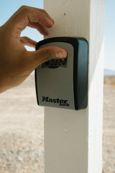 Hand operating a combination lockbox outdoors, emphasizing security and safety.