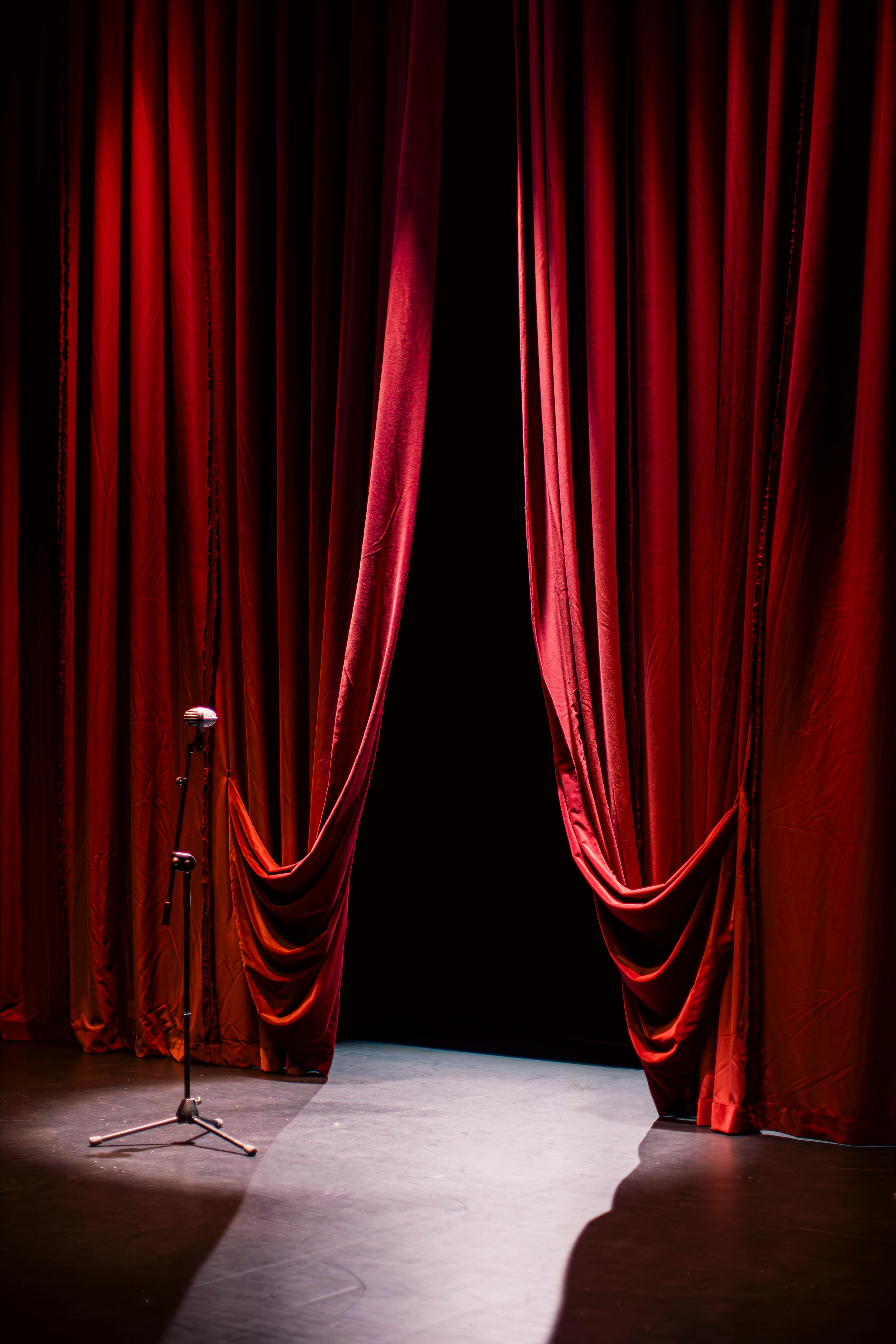 De franc Un escenari de teatre amb cortines vermelles tancades i un únic micròfon en el punt de mira, creant un ambient dramàtic. Foto d'estoc