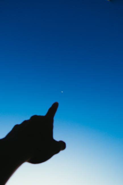 From below of crop hand pointing at lonely glowing star in dark blue sky in evening time