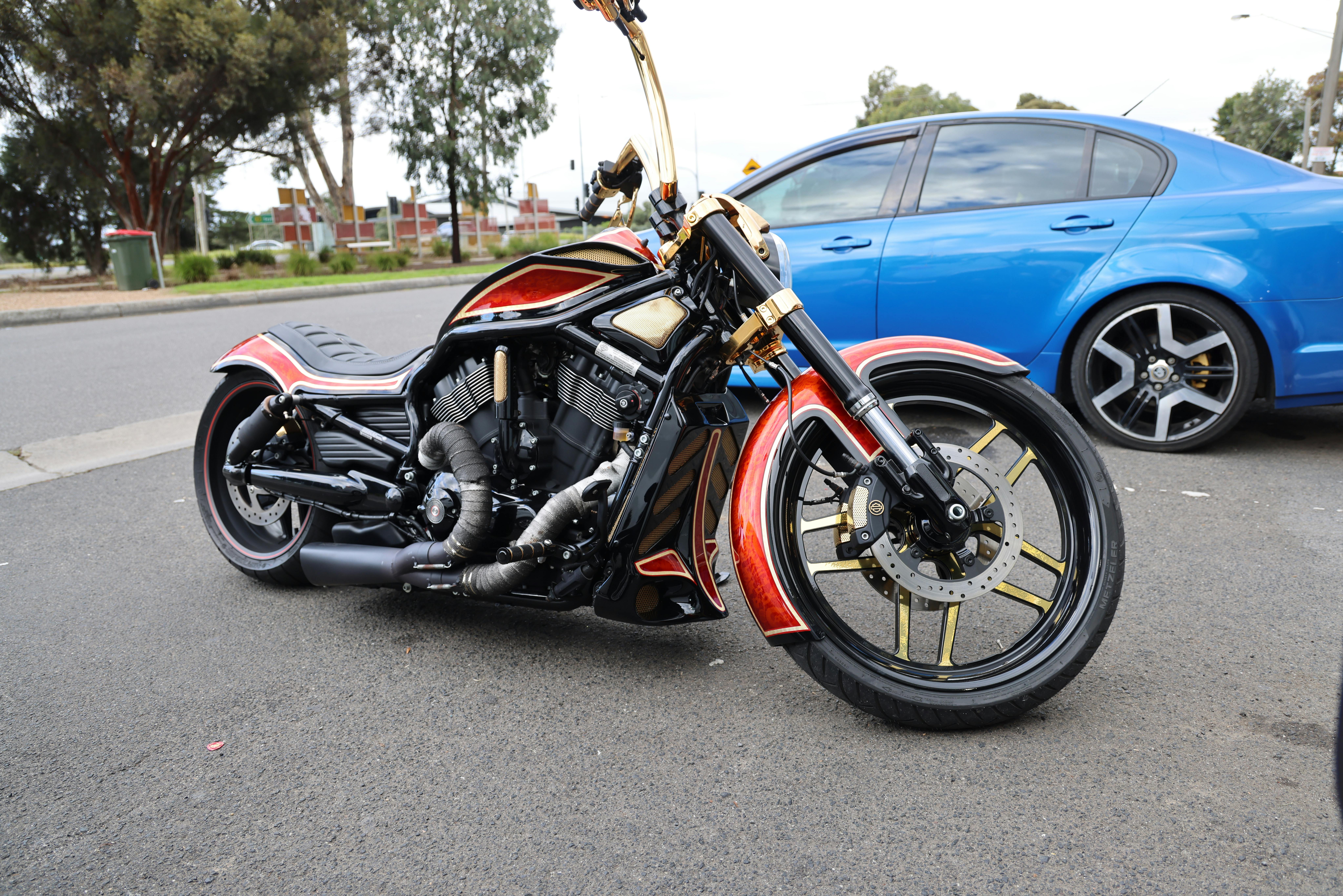 Striking custom black motorcycle with sleek red accents parked by a blue car on a city street.