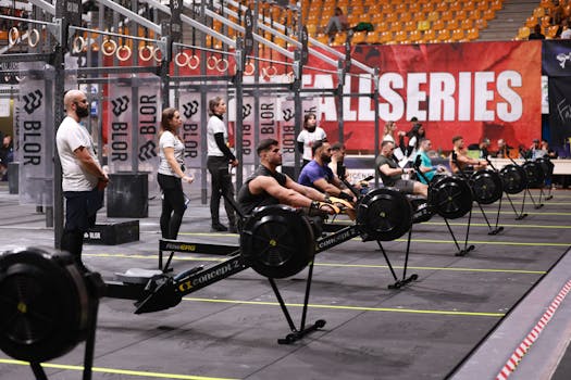 Competitors row on machines during an indoor fitness event. Focus on teamwork and endurance.