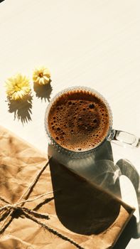 Top view of coffee cup with yellow flowers and brown paper. Cozy and warm vibe.
