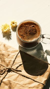 Glass coffee cup with flowers and kraft paper in warm sunlight