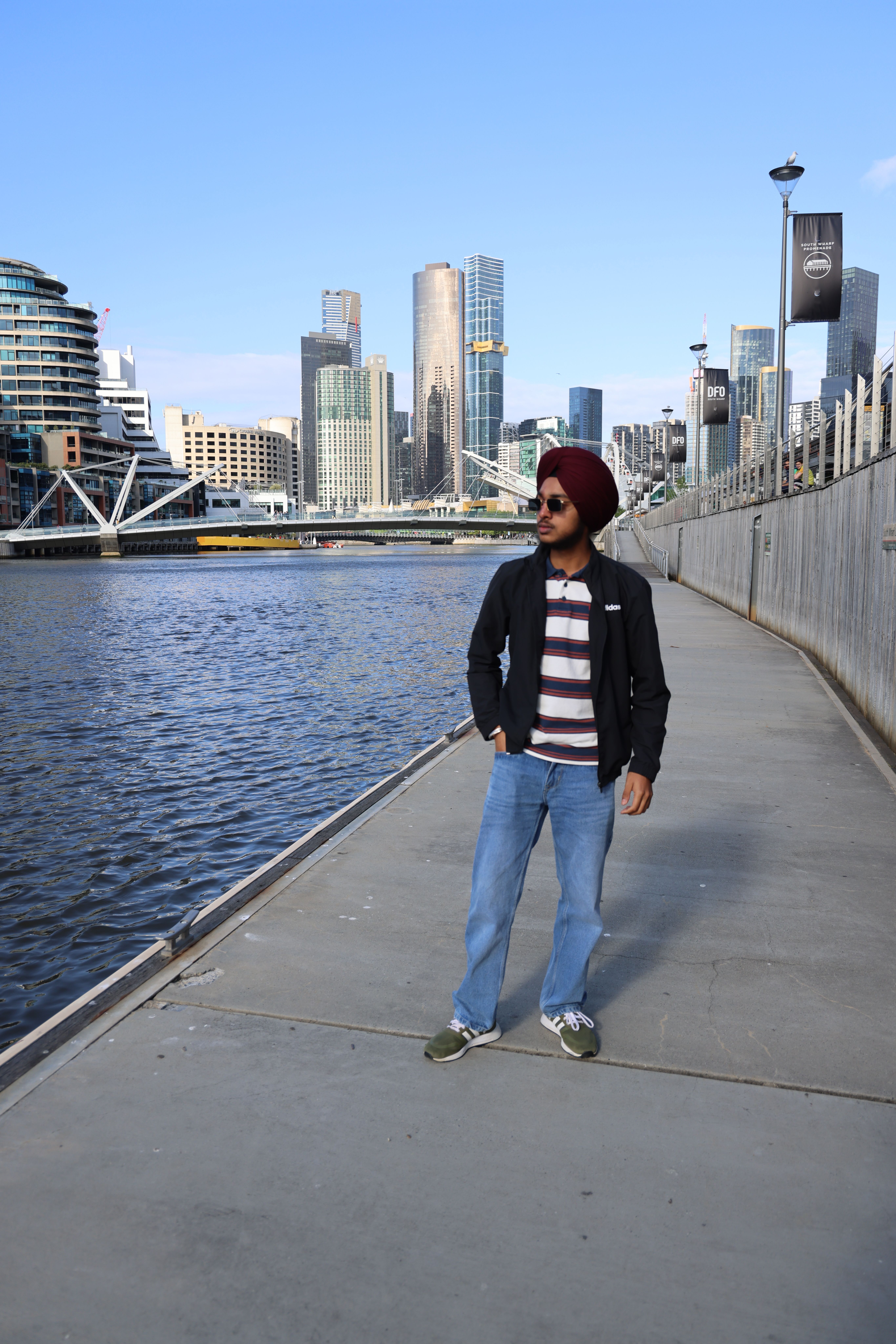 Young man posing by the Yarra River in Melbourne, with city skyline in the background.
