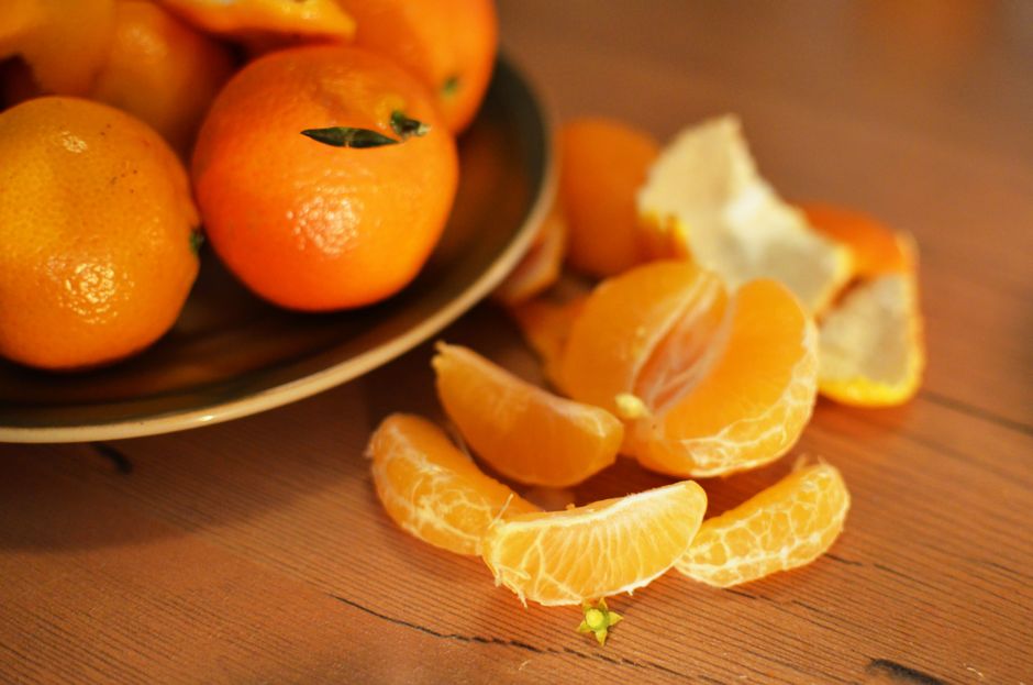 A close-up of fresh oranges and peeled tangerines on a wooden table, highlighting their vibrant color and juicy texture.
