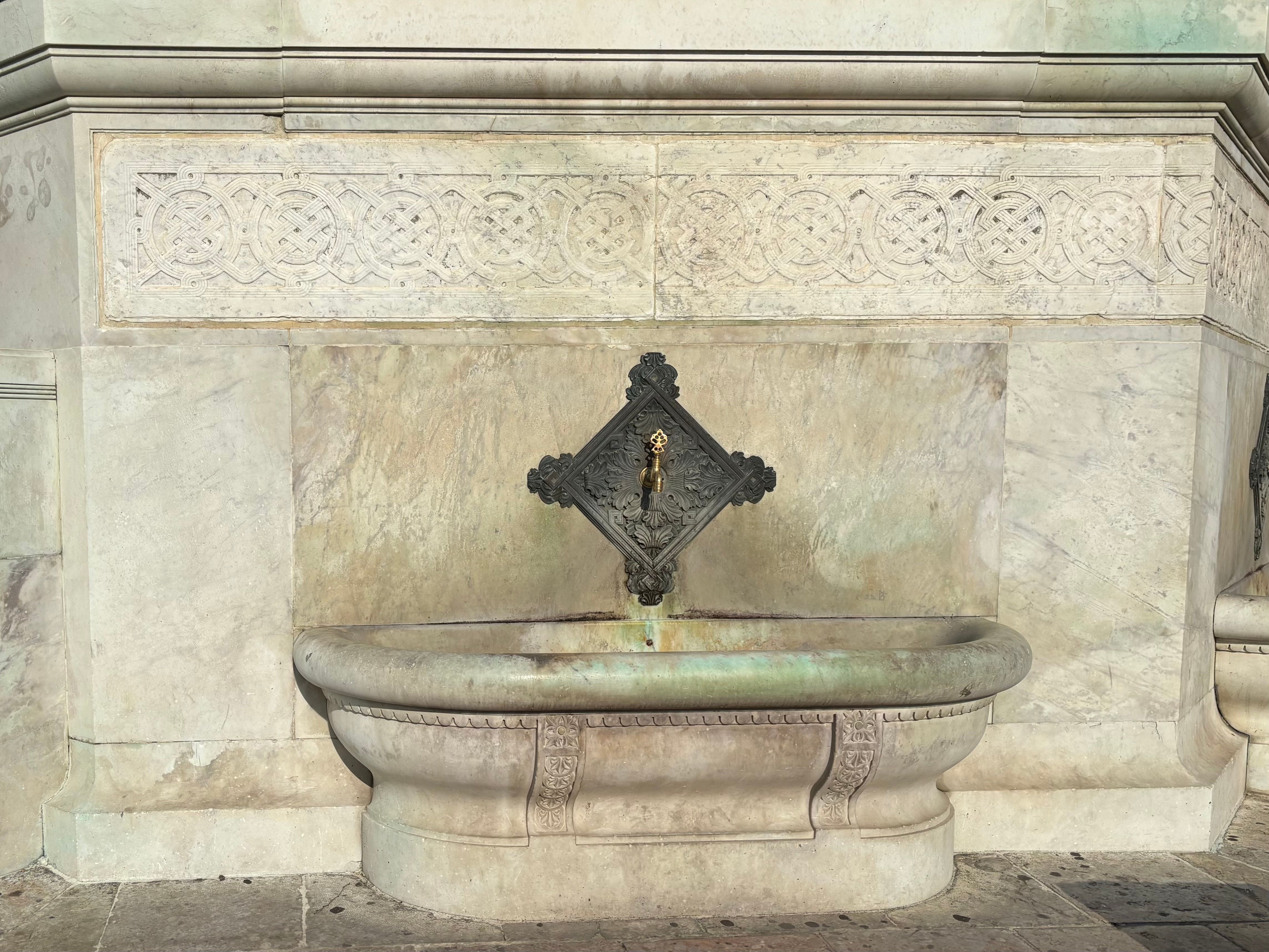 Elegant stone fountain with intricate carvings and antique metal faucet.