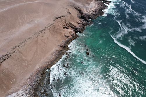 Free Stunning aerial shot of rocky coastline meeting turquoise ocean waves in the Antofagasta region. Stock Photo