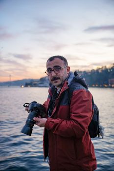 Photographer with a camera by the waterfront during sunset, capturing the serene moment.
