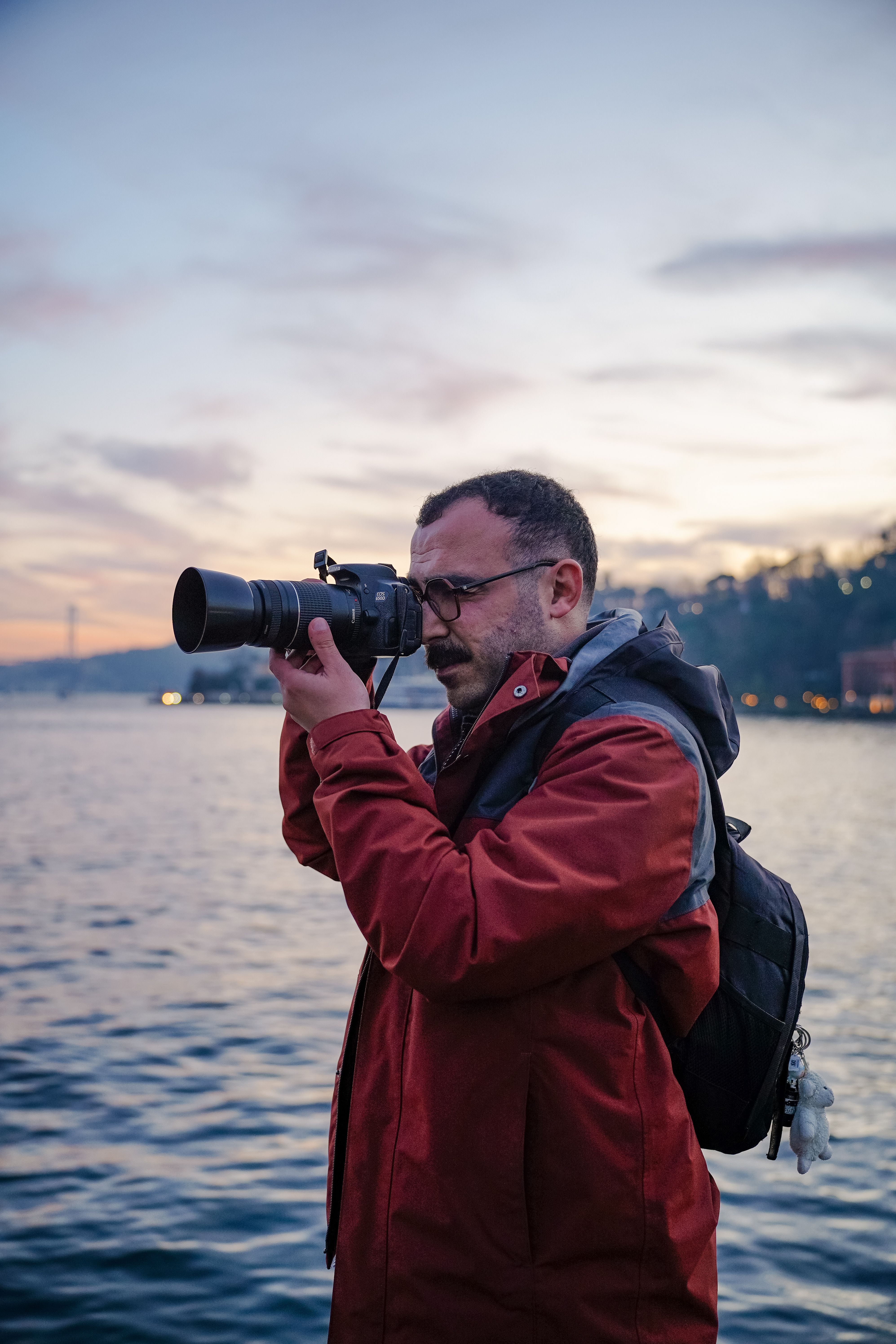Photographer takes pictures by the waterfront during sunset, capturing the scenic view with a DSLR camera.