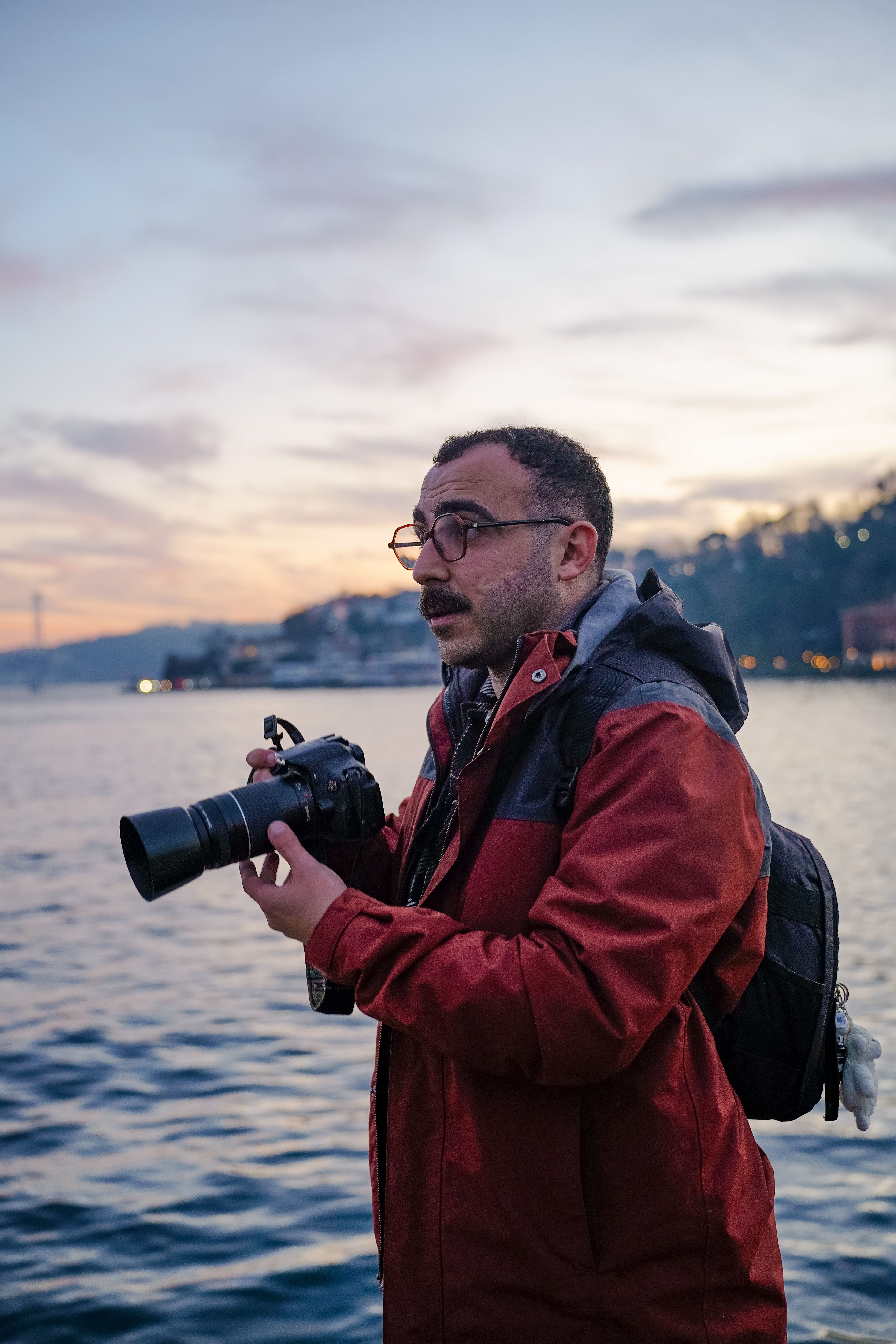 Photographer with camera at sunset by the water, capturing the serene scene.