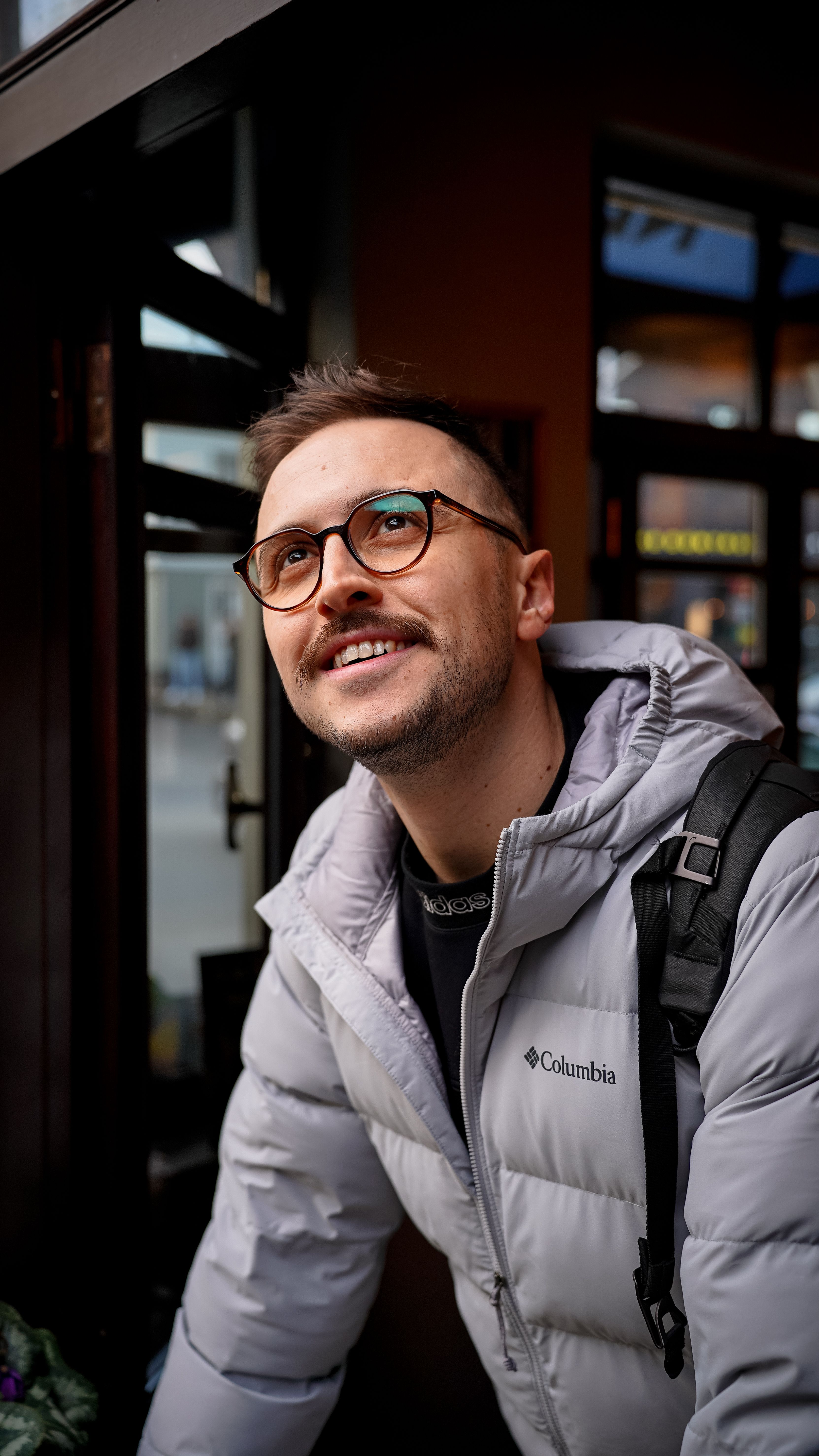 A man with glasses smiling while wearing a winter jacket outdoors.