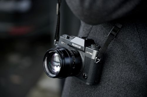 Free Detailed shot of a Fujifilm X-T30 camera hanging from a person's neck in a grey coat. Stock Photo