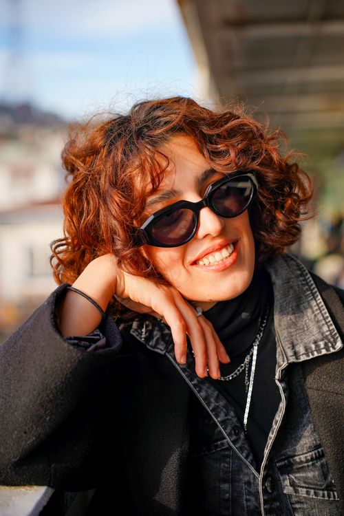 Free A stylish woman with curly hair and sunglasses smiling outdoors. Stock Photo