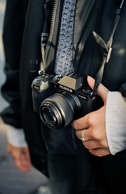 Free Person holding a Fujifilm X-S10 camera outdoors, capturing the moment. Stock Photo